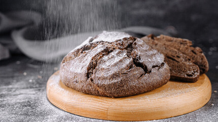 Dark round bread on the table is sprinkled with flour on top