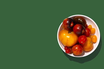 Colorful yellow, red, black tomatoes in a white plate on green background, top view