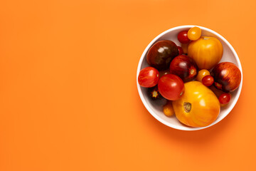 Colorful yellow, red, black tomatoes in a white plate on orange background, top view