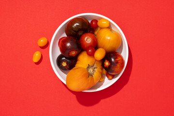 Colorful yellow, red, black tomatoes in a white plate on red background, top view