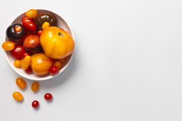 Colorful yellow, red, black tomatoes in a white plate on white background, top view