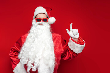 santa claus in red glasses shows his hands up on colored background, man in hat and santa costume for christmas