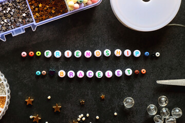 Friendship bracelet letter beads and various other jewelry making supplies on dark background. Top...