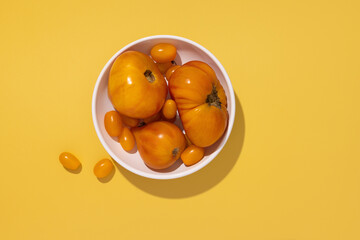 Colorful yellow tomatoes in a white plate on yellow background, top view