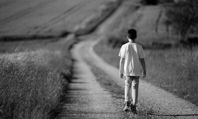 boy goes away. Teenage boy with backpack walking away on the rural road. 8 Year old boy walking...
