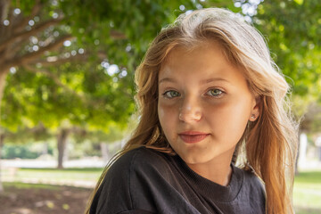 portrait of a teenage girl with blond hair, the girl sits in the park and looks at the camera
