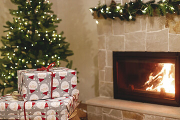 Stylish wrapped christmas gifts, christmas tree with festive lights and cozy burning fireplace. Atmospheric Christmas eve, holiday time. Merry Christmas!