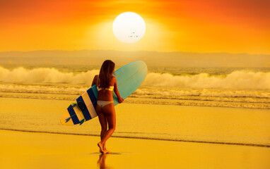 Surfer woman on the beach at sunset. Surfer girl with her back turned walking towards the waves. 