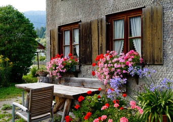 Fototapeta na wymiar traditional Bavarian alpine country house covered with wood shingles with geraniums on window ledge in the Bavarian Alps on September day in Unterjoch, Gemeinde Oberjoch, Bavaria, Germany