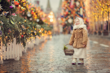 Little russian girl wearing shawl and fur coat on christmas market with lights on background 