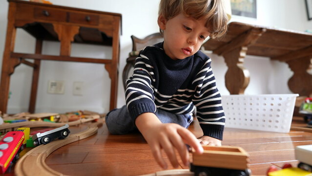 Small boy playing with car toys on hardwood floor. Child plays by himself with traditional toy on tracks