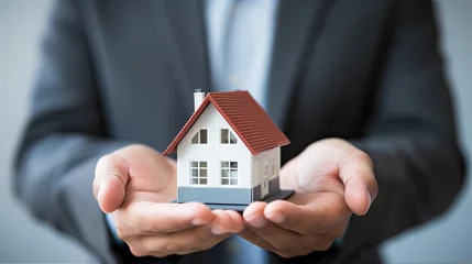 Gordijnen A businessman in a suit holds a model of a house on his palms. The concept of mortgage lending, real estate insurance, construction, design and sale of residential buildings. Illustration for design. © Login