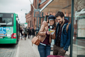 Young couple traveling and looking for directions on a map while waiting for the bus at the bus stop
