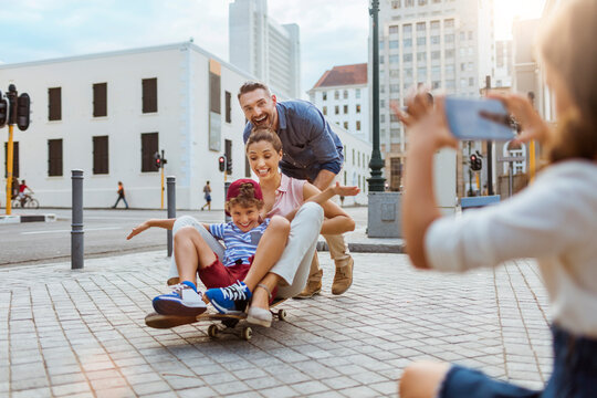 Young family having fun with a skateboard in the city and taking pictures with a smartphone