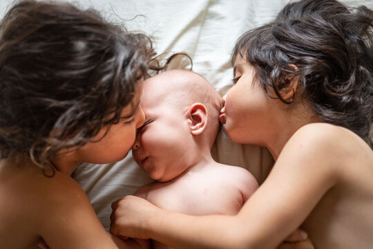 two elder children kissing perplexed newborn baby