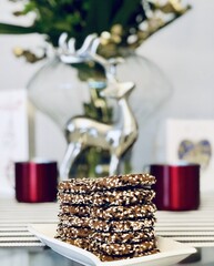 Christmas homemade thin chocolate cookies with seeds on the top presented in a small square dish with a red hot drink cup next to a Christmas silver deer figure.