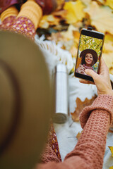 Top view of woman in hat taking selfie on her phone while enjoying time in cozy autumn park. Focus on picture in smartphone