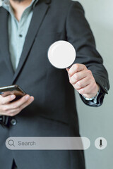 Unrecognizable man in suit holding a magnifying glass and smartphone to do an online search. Internet business technology and website traffic. Online search engine.