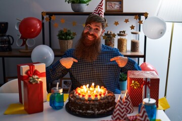 Caucasian man with long beard celebrating birthday holding big chocolate cake looking confident with smile on face, pointing oneself with fingers proud and happy.