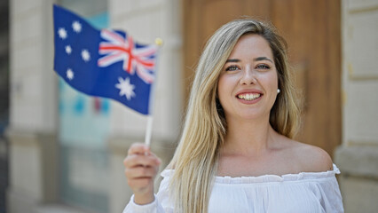 Young blonde woman smiling confident holding australia flag at street