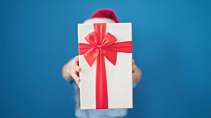 Young beautiful hispanic woman holding christmas gift over isolated blue background