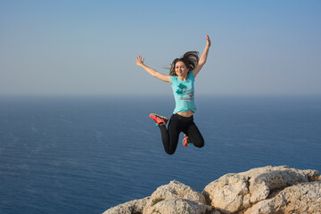 The woman jumps on the edge of the cliff. Sea in the background