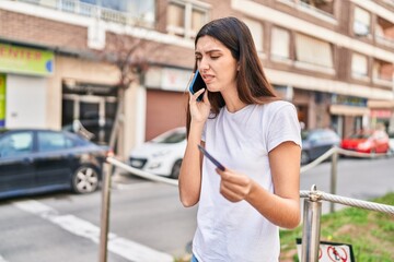 Young beautiful hispanic woman using smartphone and credit card at street