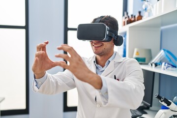 Naklejka premium Young hispanic man scientist using virtual reality glasses at laboratory