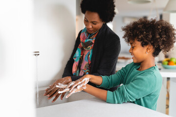 Mother and daughter washing hands with soap in a sink.