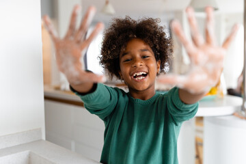 Playful African American girl smiling at camera and showing hands with soap on.