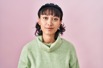 Young beautiful woman standing over pink background relaxed with serious expression on face. simple...