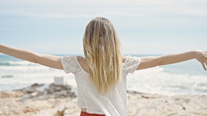 Fototapeta na wymiar Young blonde woman tourist standing with arms open backwards at beach