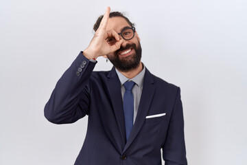 Hispanic man with beard wearing suit and tie doing ok gesture with hand smiling, eye looking through fingers with happy face.