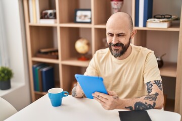 Young bald man using touchpad sitting on table at home