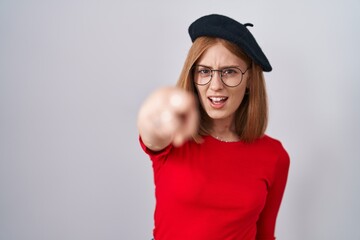 Young redhead woman standing wearing glasses and beret pointing displeased and frustrated to the camera, angry and furious with you