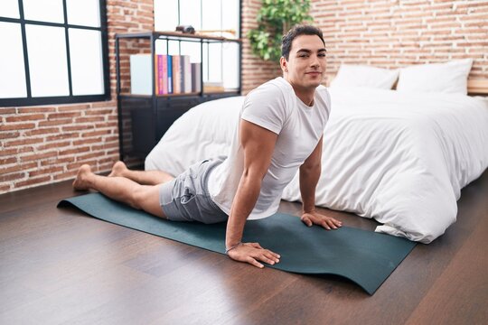 Young Hispanic Man Stretching Back Sitting On Floor At Bedroom