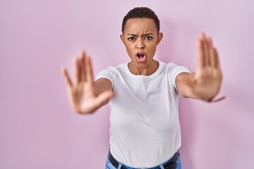 Beautiful african american woman standing over pink background doing stop gesture with hands palms, angry and frustration expression