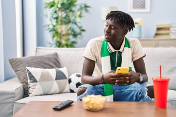 African american man supporting soccer team using smartphone at home