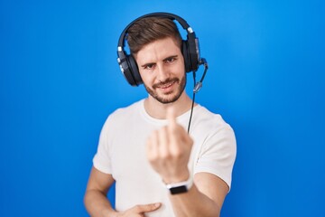 Hispanic man with beard listening to music wearing headphones beckoning come here gesture with hand inviting welcoming happy and smiling
