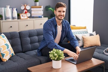 Young caucasian man using laptop sitting on sofa at home
