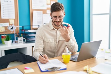 Young caucasian man business worker talking on smartphone writing on paperwork at office