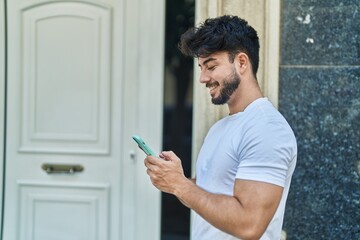 Young hispanic man smiling confident using smartphone at street