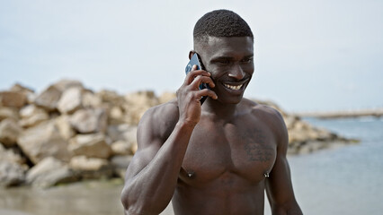 African american man tourist standing shirtless talking on smartphone at the beach