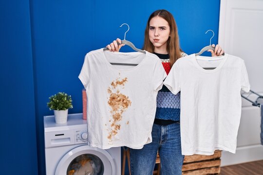 Young hispanic girl holding clean white t shirt and t shirt with dirty stain puffing cheeks with funny face. mouth inflated with air, catching air.
