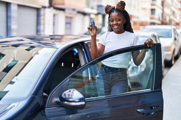 Naklejka premium African american woman smiling confident holding key of new car at street