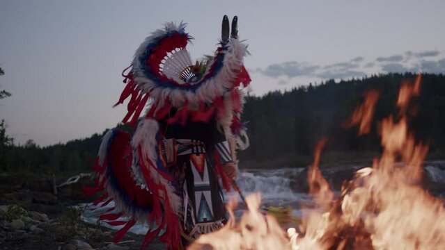 Native American Indigenous Dancing by the fireplace at sunset in Alberta Canada wearing traditional Tsu'Tina Fancy Dance Regalia. Cinematic Footage of Indigenous Fancy Dance at Sunset in Slow motion.