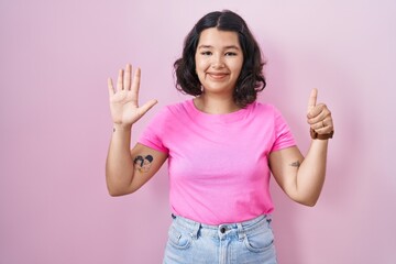 Young hispanic woman standing over pink background showing and pointing up with fingers number six while smiling confident and happy.