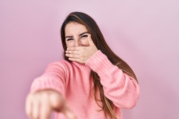 Young hispanic woman standing over pink background laughing at you, pointing finger to the camera...