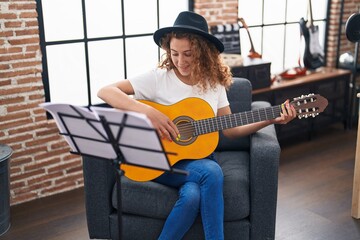 Young beautiful hispanic woman musician playing classical guitar at music studio