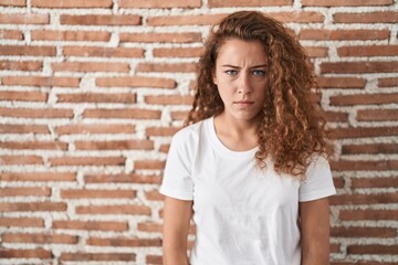 Young caucasian woman standing over bricks wall background skeptic and nervous, frowning upset because of problem. negative person.